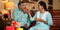 daughter-and-father-eating-sweets-by-sharing-together-at-home-during-diwali-festival-celebration-at-home